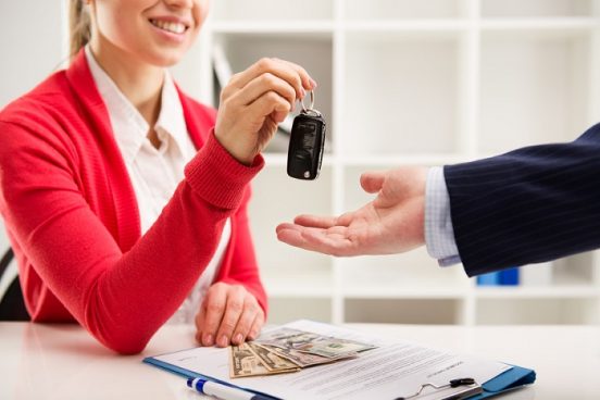 Image of a woman in a red sweater handing a car key to a customer.