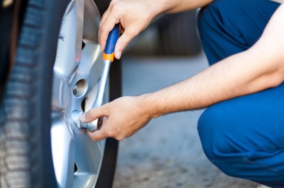 Cles-up image of a man kneeling next to a car tire and working on it with a wrench.