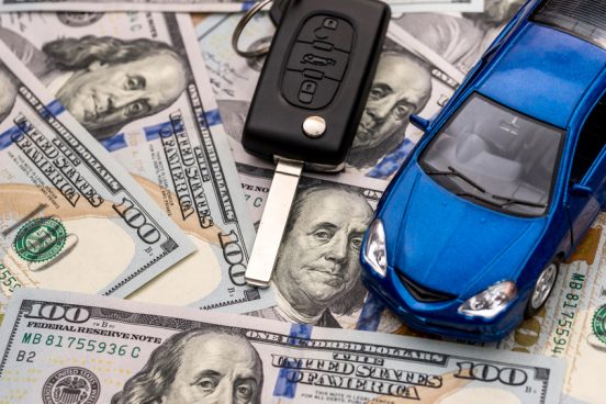 Image of a blue toy car and car keys sitting on a bunch of $100 bills.