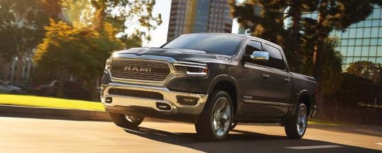 Image of a 2019 RAM 1500 driving in the sunlight on a city street.